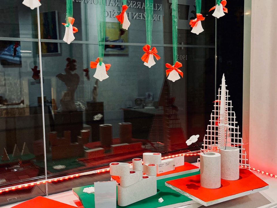 Božićno uređenje izloga Galerije Jakšić u crveno-zelenoj boji s kamenim borovima i blagdanskim detaljima